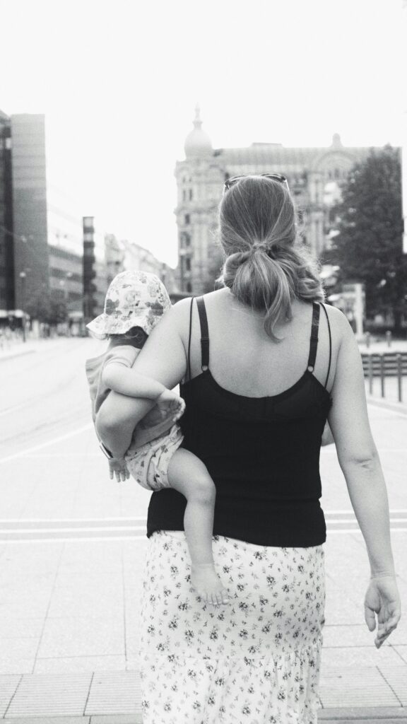 czarno białe zdjęcie, mama tyłem idąca z dzieckiem pod pachą