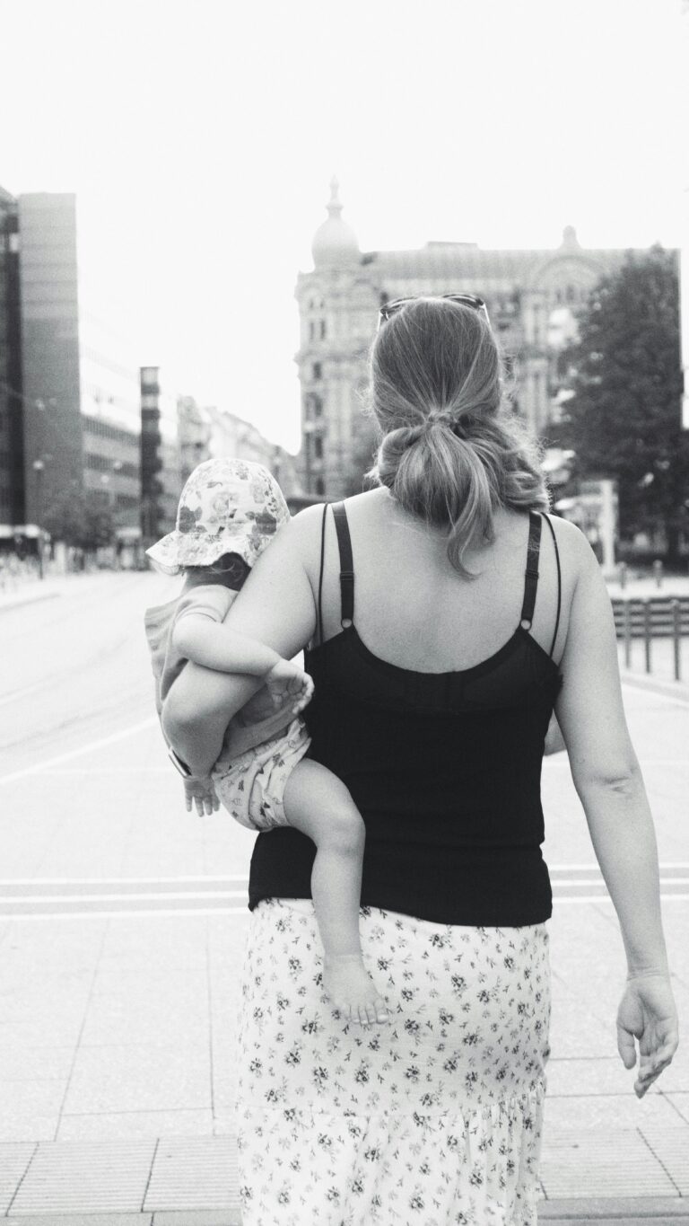 czarno białe zdjęcie, mama tyłem idąca z dzieckiem pod pachą